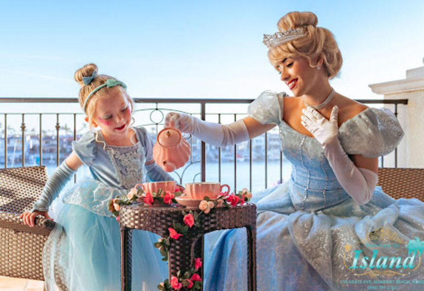 A princess pouring tea with a little girl on a Newport Beach balcony