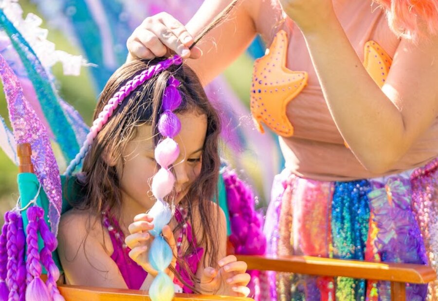 A mermaid braiding colorful bubble braids into a child’s hair